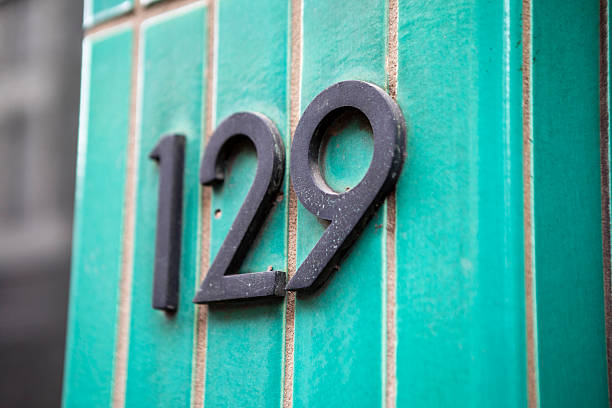 Brass number 5425 on an exterior wall mounted on the cladding identifying the property and address in an oblique angle view