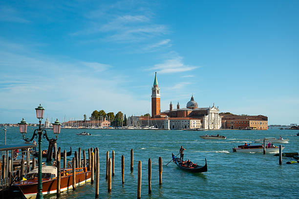 Venice, Italy - September 23, 2023: Tourists enjoying a traditional gondola ride on the grand canal, with the iconic san giorgio maggiore church and bell tower dominating the background under a clear blue sky