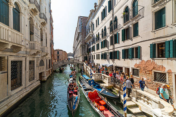 Venice, Italy - September 24, 2023: Tourists stroll and ride gondolas along a sunlit venetian canal, passing historic buildings and arched bridges in a picturesque summer city scene of culture and sightseeing