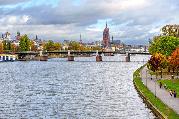 Frankfurt, Germany - October 21, 2025: Expansive view of Frankfurt's Main River, featuring the Eiserner Steg, the cathedral, and historic buildings along the autumnal riverfront.