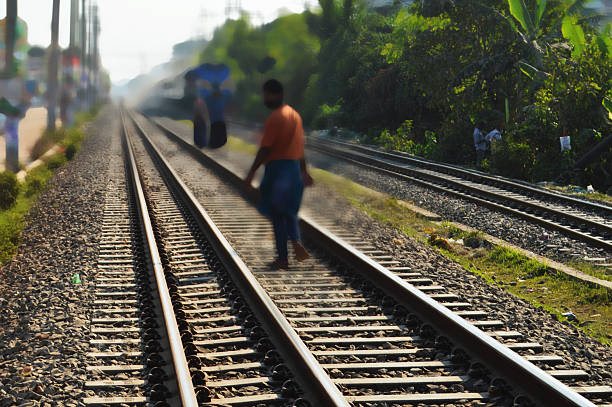 People Walking Along Railway Tracks as a Train Passes by in Lush Green Landscape
