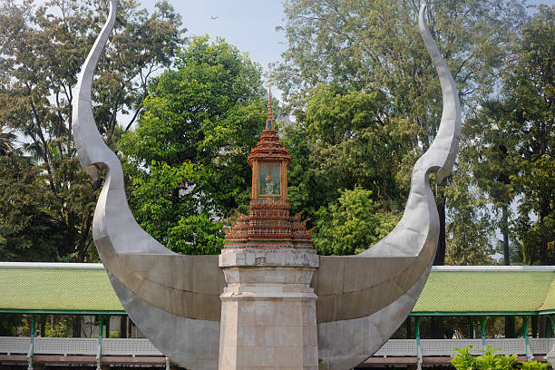 Thai buddhist sculpture on campus of Kasetart University in Bangkok. Sculpture is located in front of Prasert Na Nagara Hall or Prasert Na Nagara Theatre.  At centered ornated structure are mnay small buddhas. Sculpture is placed in a pond. In background are trees behind the pond. Artisyt is unknown