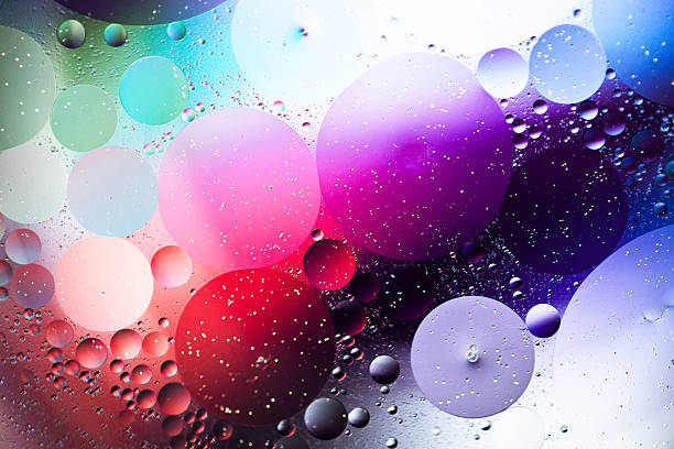 Close up macro image depicting droplets of oil in water on a multi colored background. The oil forms interesting circles and spheres in the water, and colorful background produces an abstract effect.