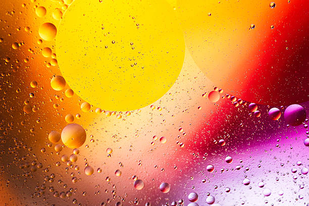 Close up macro image depicting droplets of oil in water on a multi colored background. The oil forms interesting circles and spheres in the water, and colorful background produces an abstract effect.