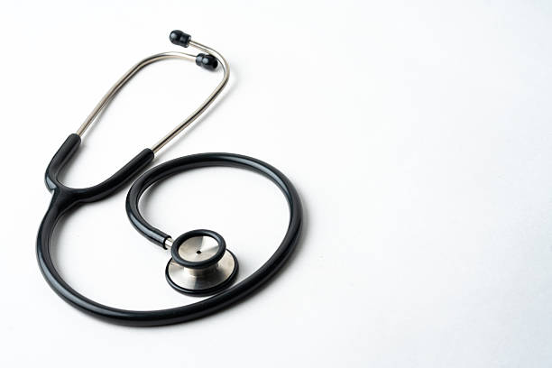 a high-angle, minimalist shot of a classic black medical stethoscope curled on a clean white surface. The image features ample negative space on the right, making it ideal for medical headlines, healthcare advertising, and insurance concepts.