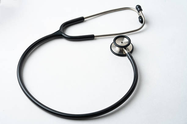 a high-angle, minimalist shot of a classic black medical stethoscope curled on a clean white surface. The image features ample negative space on the right, making it ideal for medical headlines, healthcare advertising, and insurance concepts.