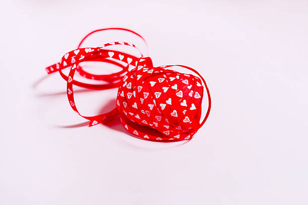 Curled red ribbon printed with small white hearts arranged on a clean pink backdrop. Bright, playful Valentine’s Day or Mother’s Day concept with copy space for text or design.