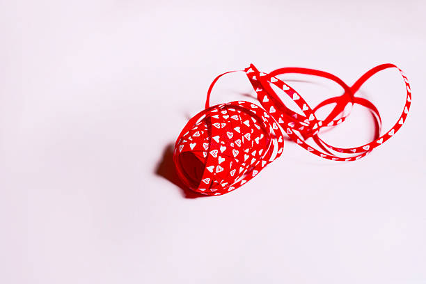 Red decorative ribbon with white heart pattern curled into a roll on a soft pink background. Minimal Valentine’s Day or Mother’s Day styling with generous copy space for greeting text, branding, or promotional message.