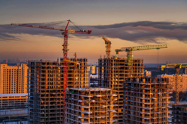 Multiple unfinished apartment buildings with visible concrete frames and tower cranes in a dense urban area during evening light. Image is suitable for illustrating residential development, construction industry, or urban growth.