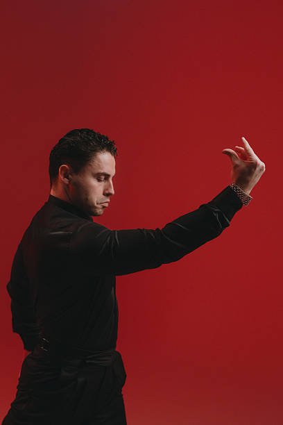 Expressive male in profile with red backdrop, delicate hand gesture, focused gaze, theatrical posture, warm directional light,