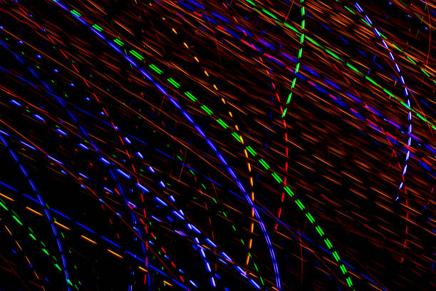 Bright light trails and spots create futuristic patterns against a dark backdrop. Abstract background with defocused lines and spots, made by glowing fiber optic lights.