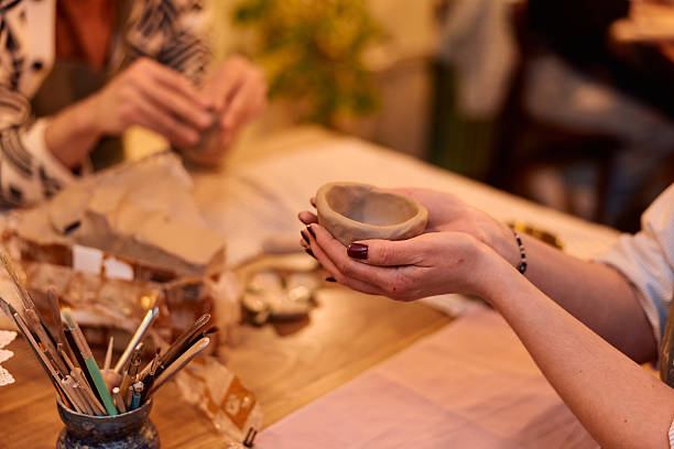 Woman holding a small heart-shaped clay bowl in her hands, showcasing a finished piece from a creative pottery workshop where participants learn ceramics as a hobby