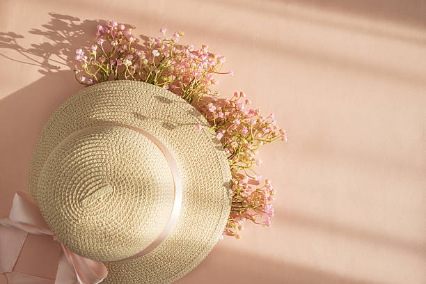 Straw Hat with Pink Ribbon and Flowers. Romantic Spring Summer Flatlay on Peach Background