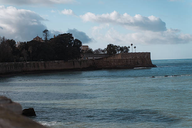 Scenic coastal panorama of Cádiz, Spain, showing the turquoise Atlantic Ocean, the city’s waterfront with historic buildings, and the prominent bridge Puente de la Constitución de 1812 in the background.