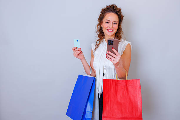 Woman making a digital purchase, standing with shopping bags and using her smartphone for e-commerce