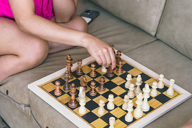 A young woman sitting on her sofa moves a chess piece during a strategic board game