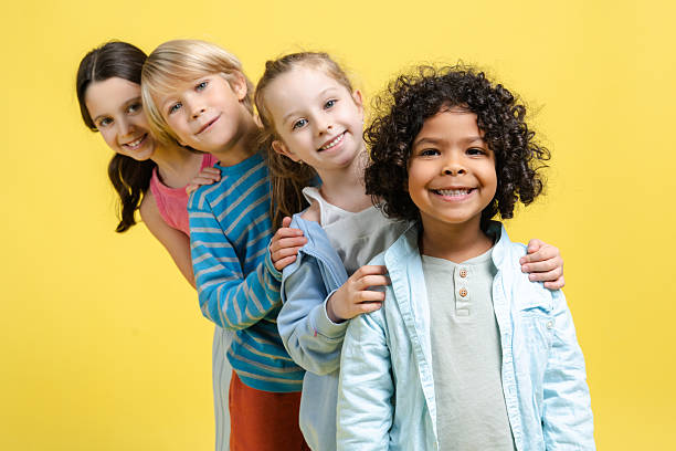 Smiling positive diverse group of happy multinational children looking at camera posing isolated on yellow background. Childhood concept