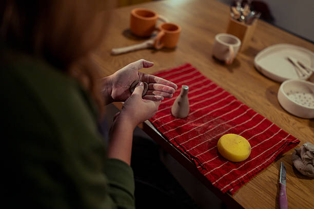 Woman engaged in the therapeutic and creative hobby of pottery. The focus is on the hands rolling and pressing a small piece of clay next to a newly formed miniature vessel