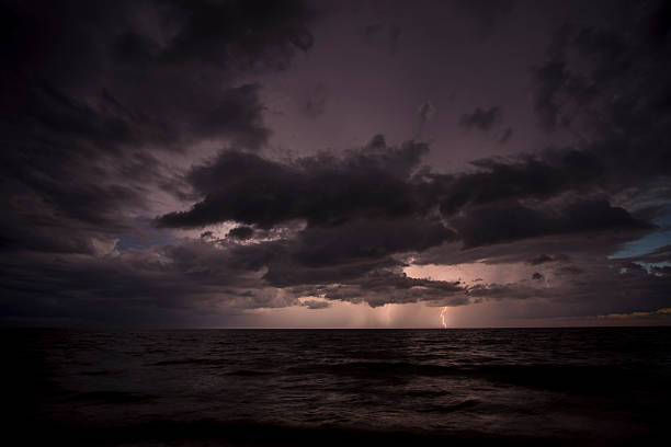 Thunderstorm dark clouds with lightning and thunder over evening sea water waves crushing on sandy beach. Seascape weather at sunset.