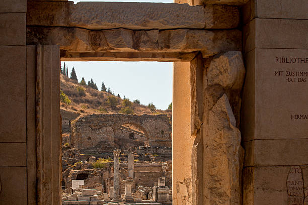 View through an ancient stone gate revealing ruins and arches of the ancient city of Ephesus, Turkey. A perspective of Roman-era architecture and history.