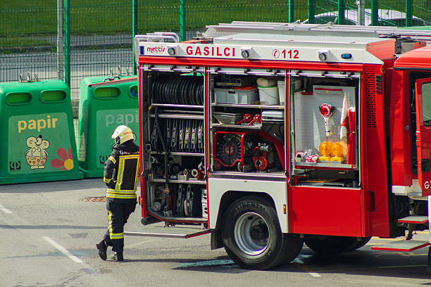 Borovnica Slovenia June 04, 2025 slovenian firefighter stands next to an open fire truck with equipment compartments fully exposed. various rescue tools, hoses, and safety gear are organized inside the vehicle. the scene captures emergency preparedness and firefighting operations in an outdoor urban setting.
