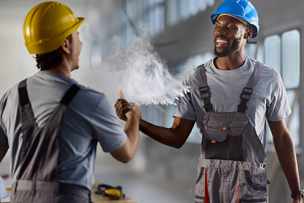 Happy African American manual worker having fun while greeting with his colleague at construction site.