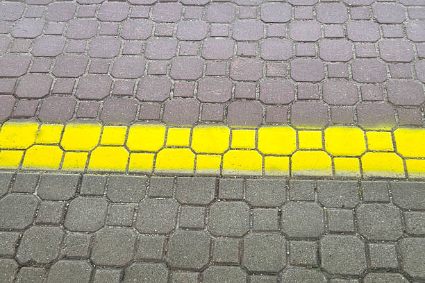 Brick pavement showcasing a distinct yellow safety line, dividing two sections of walkway. the geometric arrangement of bricks highlights urban design and safety measures, emphasizing pedestrian areas and traffic guidance.
