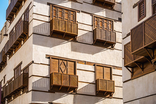 Sunlit historic buildings featuring intricately designed wooden balconies in Jeddah Al Balad old town. The architecture reflects traditional elements with detailed lattice designs and cultural significance in the urban landscape.