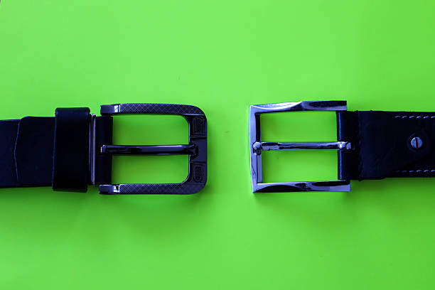 A comparative view of two different metal belt buckles arranged horizontally on a bright lime green background. Demonstration of differences in design and texture of classic chrome hardware for leather accessories in modern product photography.