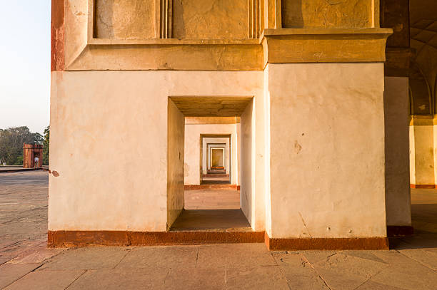 Agra, India - March 12, 2024: The image shows an exterior view of a colonnaded corridor at Akbar's Tomb, featuring a series of rectangular arches and thick pillars in warm sunlight, with stone paving and part of the complex visible outside.