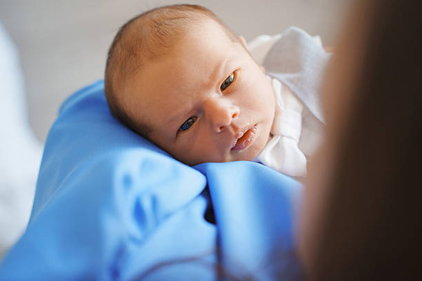 A baby lays on a blue cloth while looking intently at a parent. The setting shows a close interaction between them. The time is daytime with soft lighting.