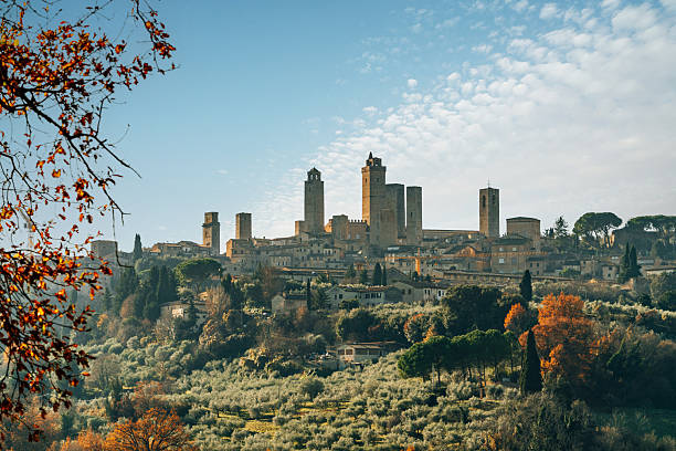 Historic San Gimignano skyline with ancient towers rising above olive groves and colorful autumn foliage under a clear blue sky