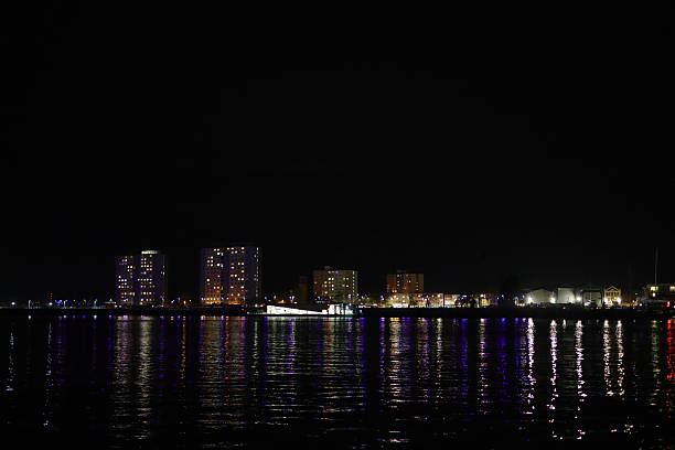 Portsmouth Harbour, Hampshire, England. 18 January 2026. Night scene: A night-time view from a ferry crossing the harbour, capturing Gosport’s illuminated waterfront. Reflections ripple beneath the pontoon and modern blocks of flats, creating a calm, colourful scene shaped by motion and shifting harbour lights.
