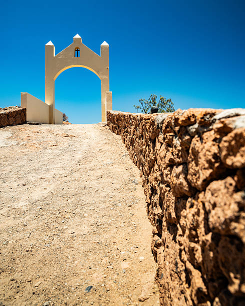 Minimalist view of a stone archway along a dirt path in Tenerife, surrounded by volcanic terrain and clear blue sky. Outdoor travel scene showcasing architecture, nature, and hiking routes in the Canary Islands.
