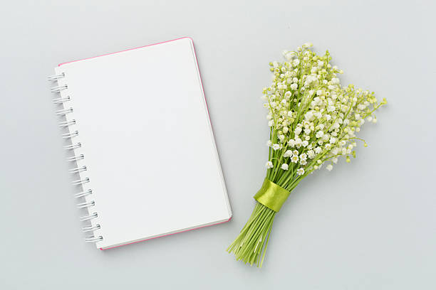 Lilies of the valley with notebook on color background, top view