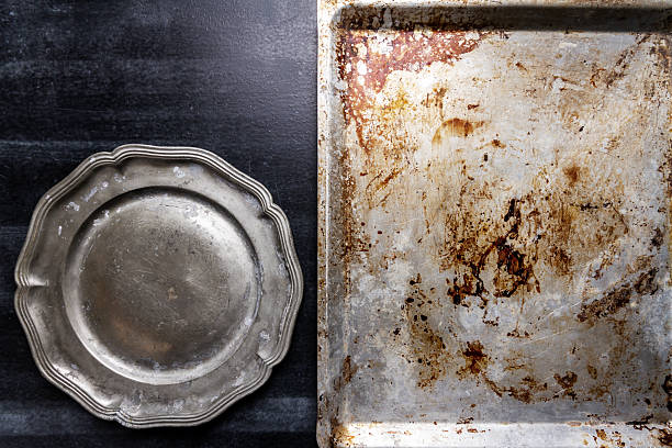 Used oven flat baking pan with burned spots and scratches and pewter plate on black chalkboard background