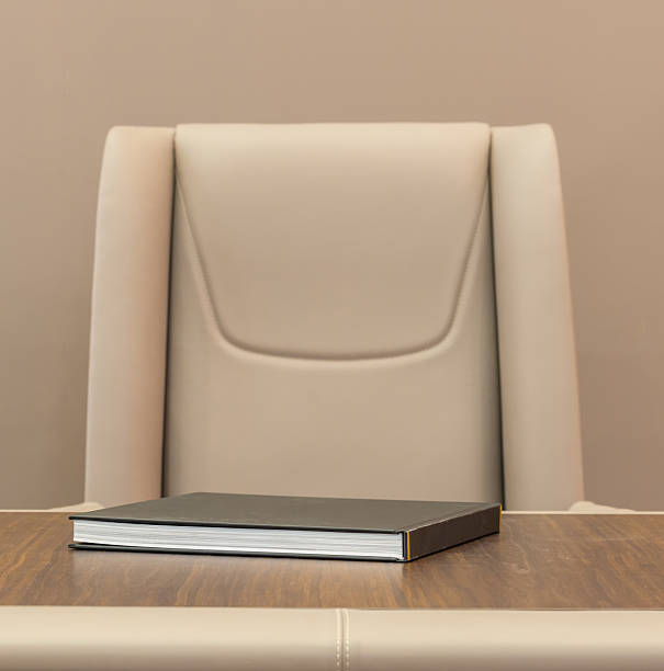 Leather chair with hardcover book on seat, closeup of textured upholstery and wood tabletop, warm neutral palette, soft ambient