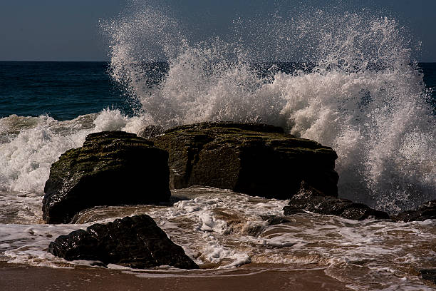 Waves break powerfully over the coastal rocks, capturing the raw interaction between water and stone. The image reflects the constant motion of the ocean and the sculpting force of nature along the shoreline.