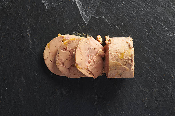 Slices of foie gras terrine arranged on dark slate, showcasing its creamy texture and delicate marbling. The image emphasizes the richness and artisanal quality of this classic French delicacy, ideal for illustrating fine dining, gourmet products, festive cuisine, and high-end food presentation.