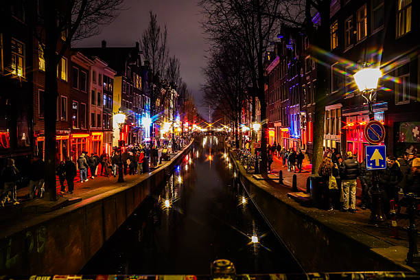 Night view of an Amsterdam canal with illuminated buildings, street lights and reflections on the water. Atmospheric city scene during winter nightlife.