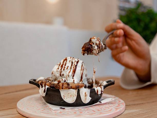 Chocolate dessert in a cast iron skillet topped with whipped cream and chocolate drizzle, restaurant dessert photography, close up, hands serving