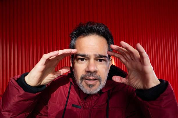Man looking through something, contemplating serious ideas against a vibrant red background.