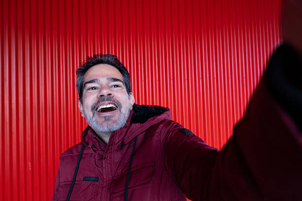 Man laughing and smiling while taking a selfie against red wall