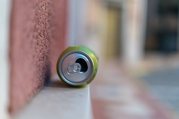 Close up of an empty aluminum beverage can lying on a sidewalk near a textured wall with shallow depth of field and urban background blur. Concept of littering and pollution