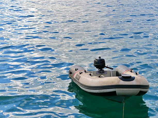 Small grey inflatable boat with black outboard motor floating calmly on the rippled, bluegreen water of a lake or sea, perfect for summer holidays and fishing.