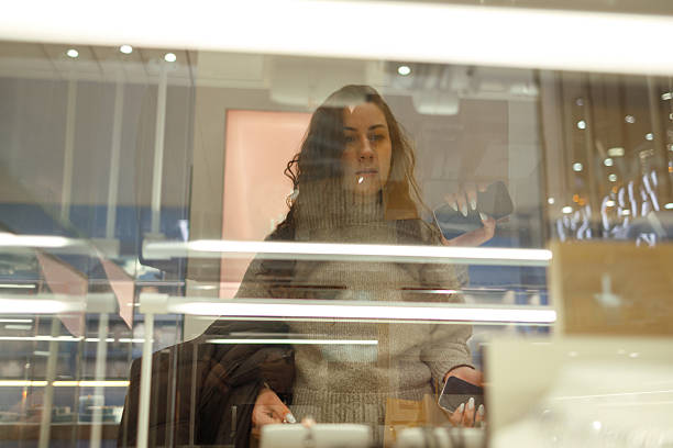 Young woman standing in a shopping mall and looking at jewelry displayed in a store window inside a retail center.