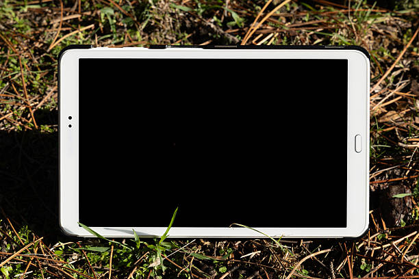 Blank screen tablet device photographed outdoors on a wooden surface in a rural setting, illustrating modern technology, remote work concepts, and contemporary rural lifestyle.