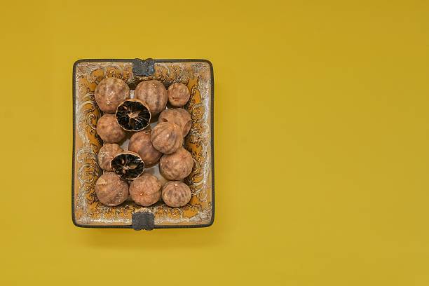 Dried black lime known as loomi arranged on yellow background with copy space. Traditional Middle Eastern spice used in Arabic and Persian cuisine for food design, recipe and packaging.
