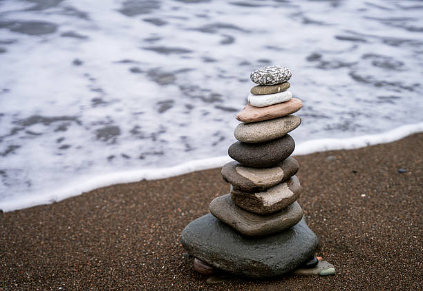 Single stack of balanced zen stones on a sandy beach with sea waves background