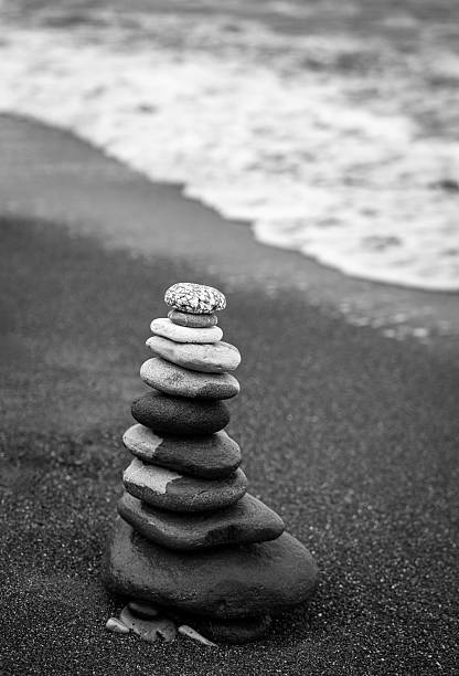 Single stack of balanced zen stones on a sandy beach with sea waves background